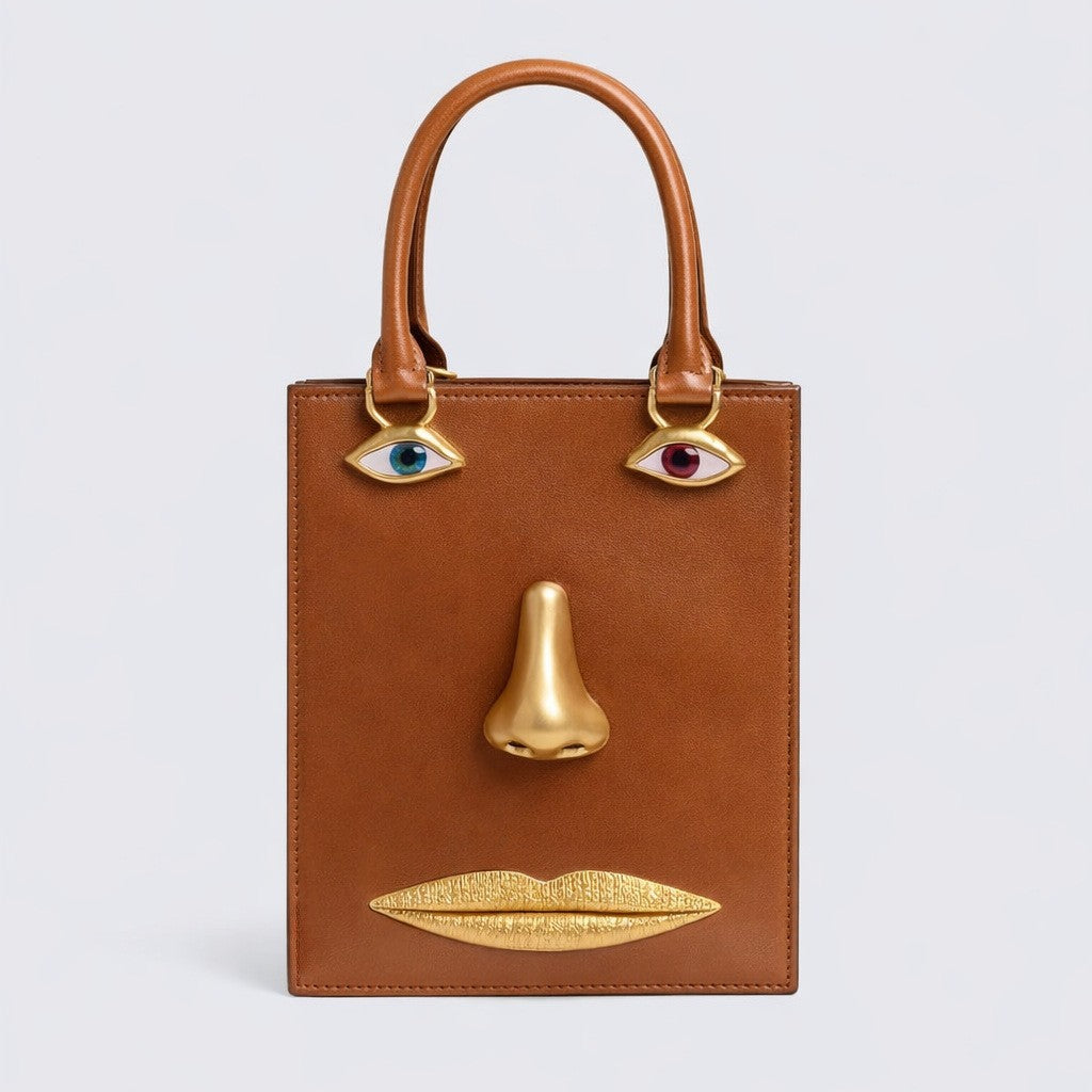 Structured rectangular top-handle bag in tan leather-look finish with gold-tone sculptural face hardware including