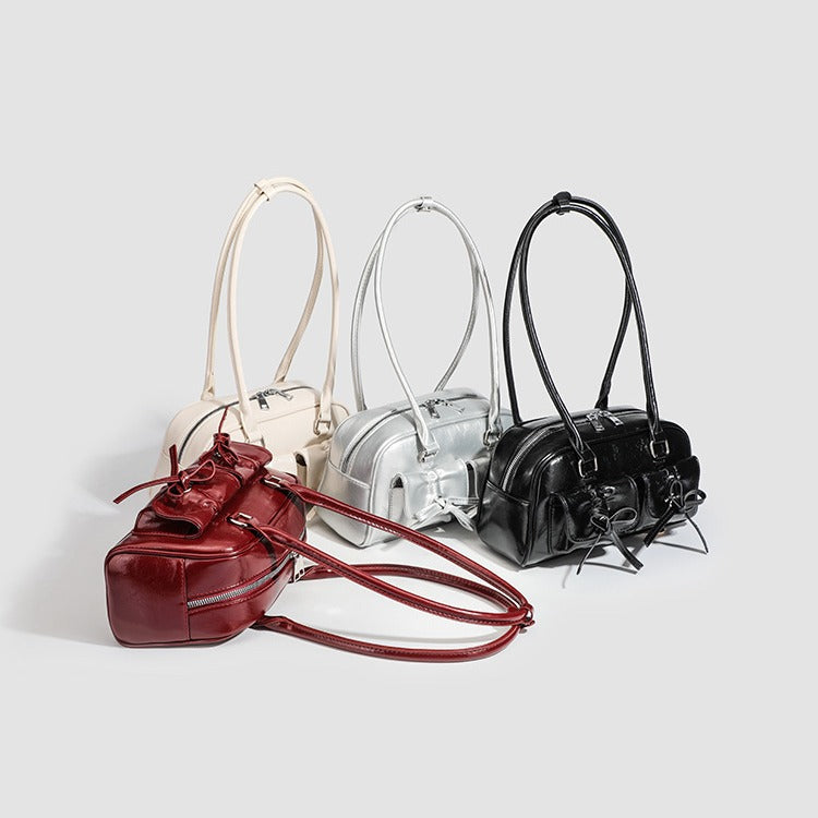 Compact glossy leather-look shoulder bag with bow-drawstring front pockets, zip-top closure, dual top handles, and, detail