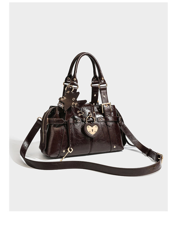Structured leather-look satchel bag with heart padlock charm, star charm, gold-tone buckle hardware, dual top handles, and