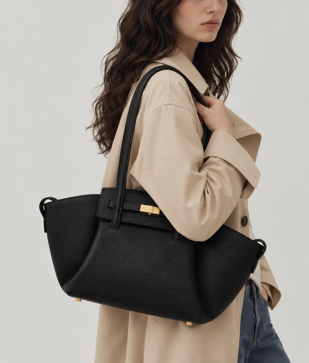 Black pebbled trapezoid tote bag with gold turn-lock hardware and double top handles, detail view 10