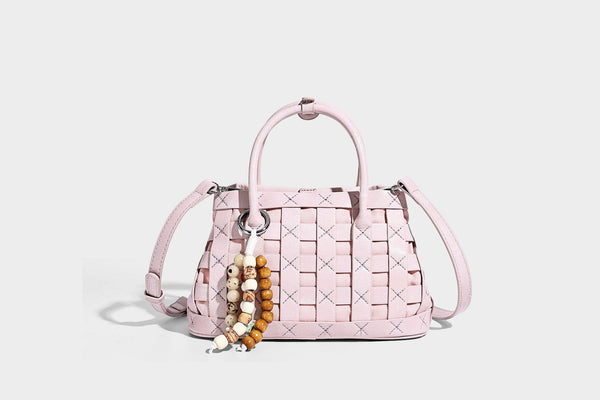 Small structured woven satchel tote with rounded top handles, silver-tone ring hardware, and bead tassel charm, detail view