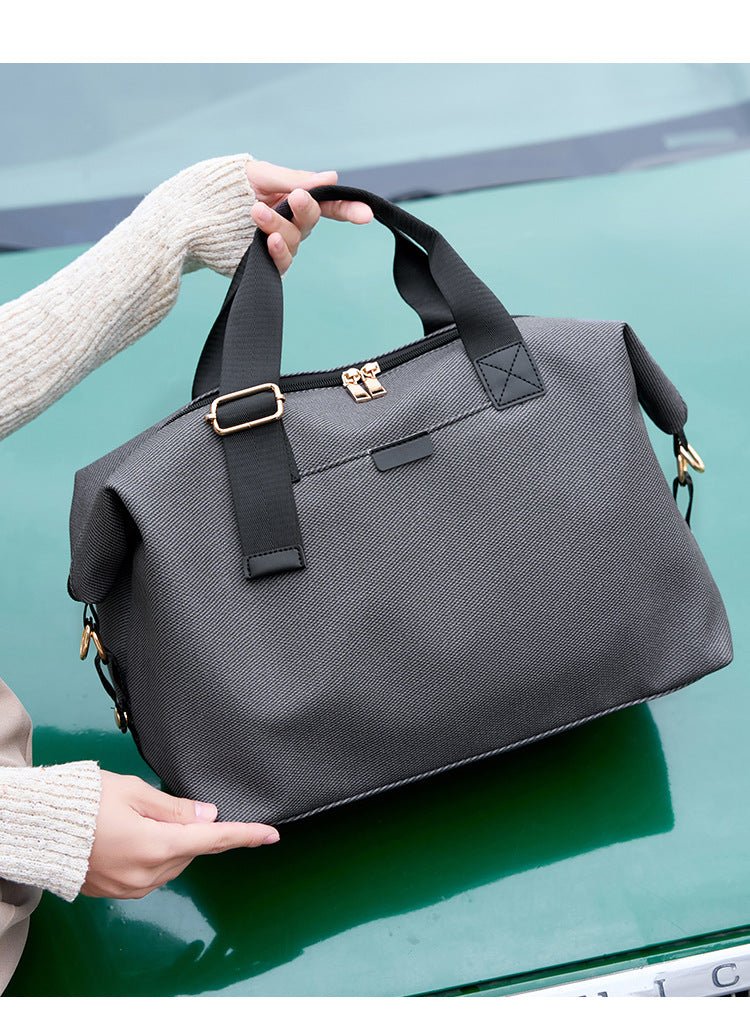Structured woven duffel bag with dual tan webbing handles, detachable shoulder strap, top zip closure, and gold-tone