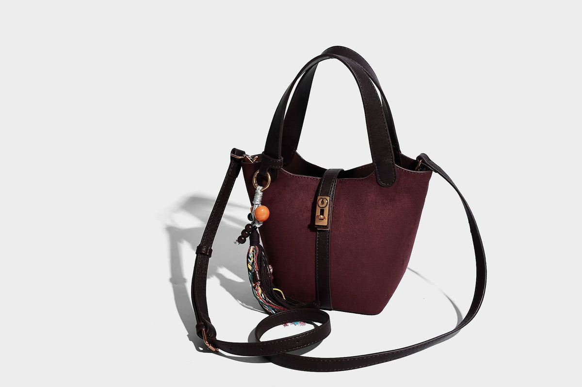 Small structured trapezoid tote bag in matte suede-look finish with black contrast trim, gold-tone front clasp, tassel charm