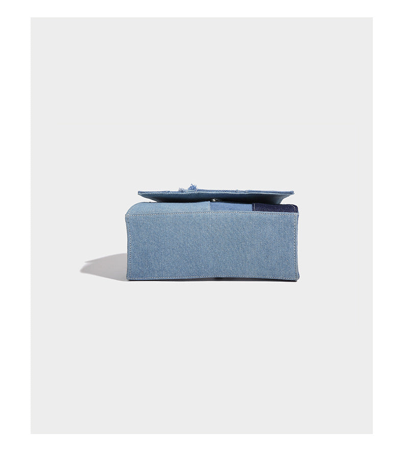 Structured patchwork denim trapezoid satchel bag with frayed panel trim, rounded top handle, and silver-tone hardware, detail