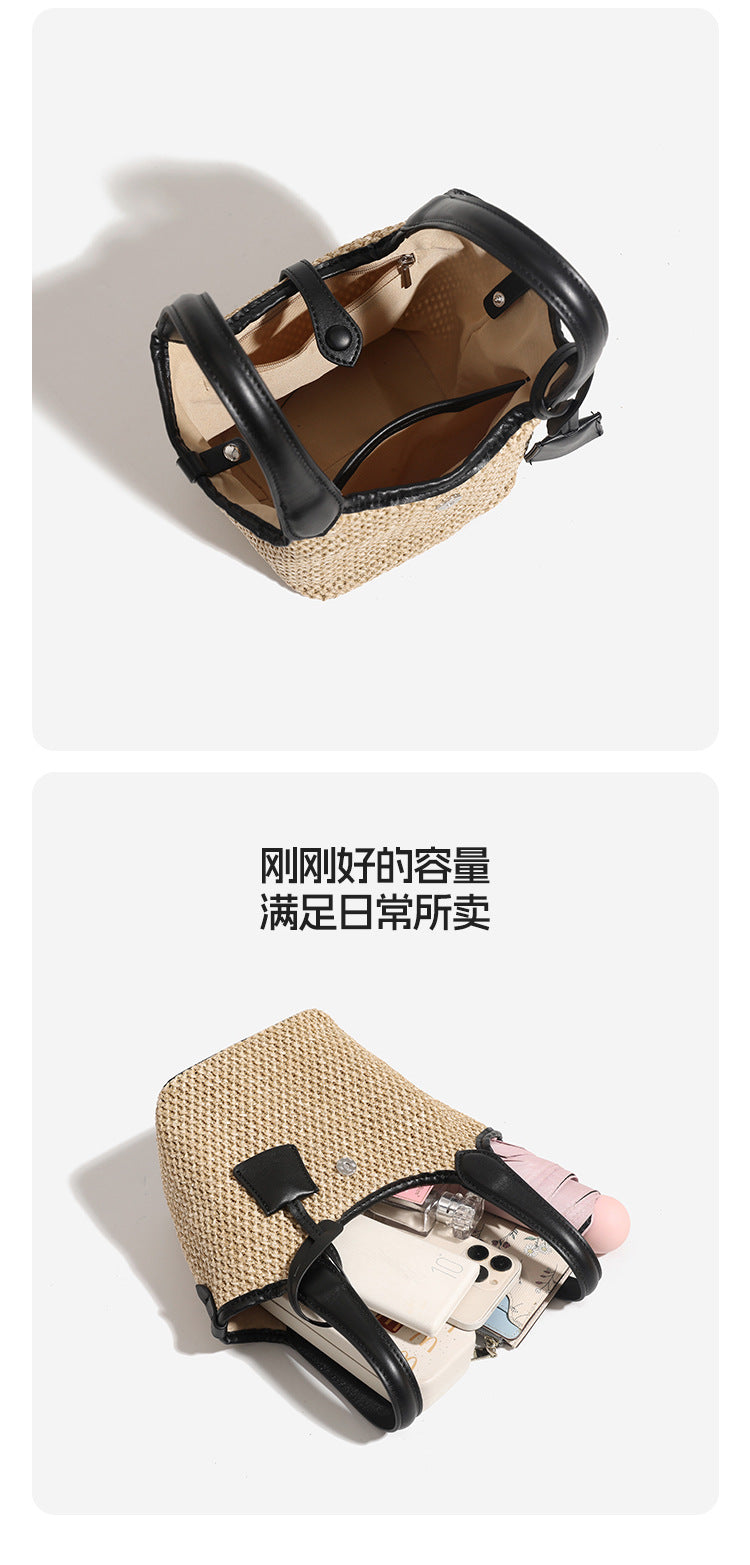 Woven beige straw bucket bag with black leather-look trim, dual top handles, detachable shoulder strap, and front snap