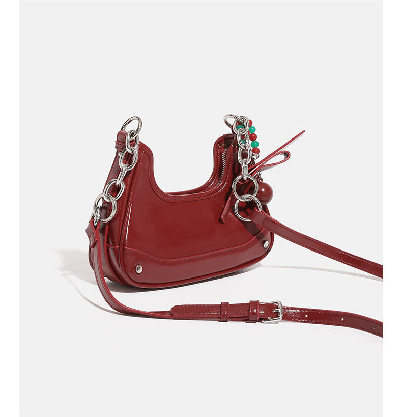 Small glossy cherry red crescent shoulder bag with silver chain strap, bead and tassel charm, and round pendant, detail view
