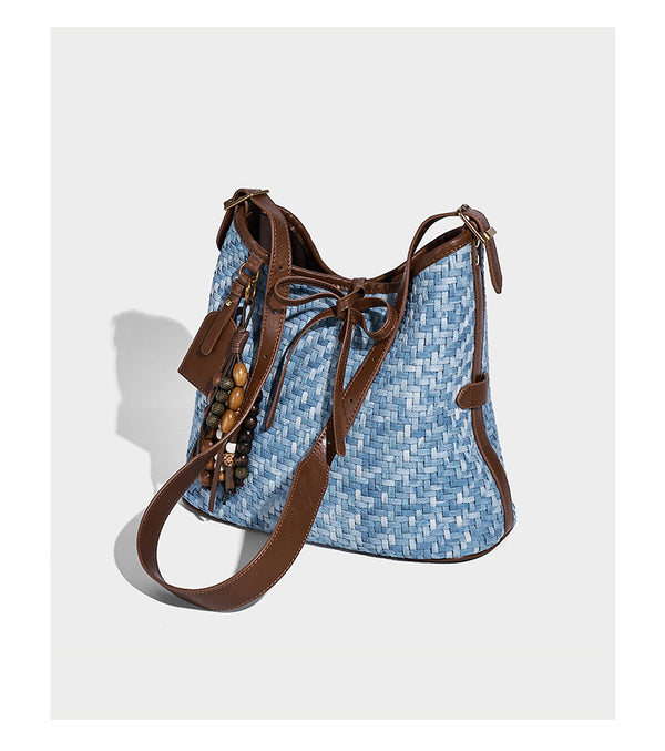 Light blue woven bucket bag with brown leather-look trim, gold-tone hardware, adjustable shoulder strap, and decorative bead