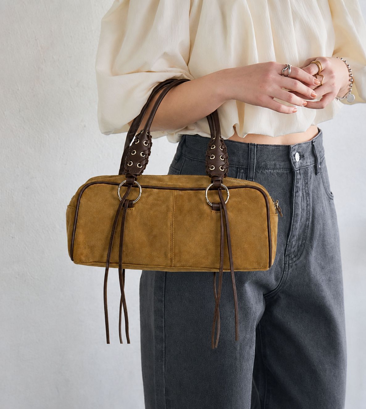 Rectangular suede-look barrel bag with laced eyelet handles, silver O-ring hardware, and hanging leather-look fringe tie