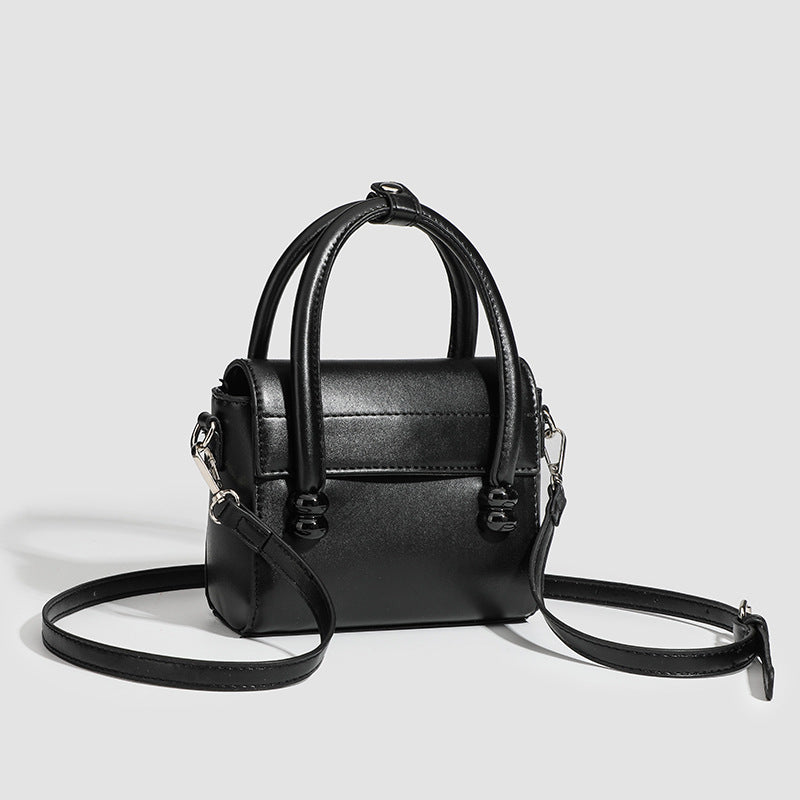 Kleine strukturierte schwarze Henkeltasche im Lederlook mit zwei abgerundeten Henkeln, abnehmbarem Umhängeriemen und silberfarbenem