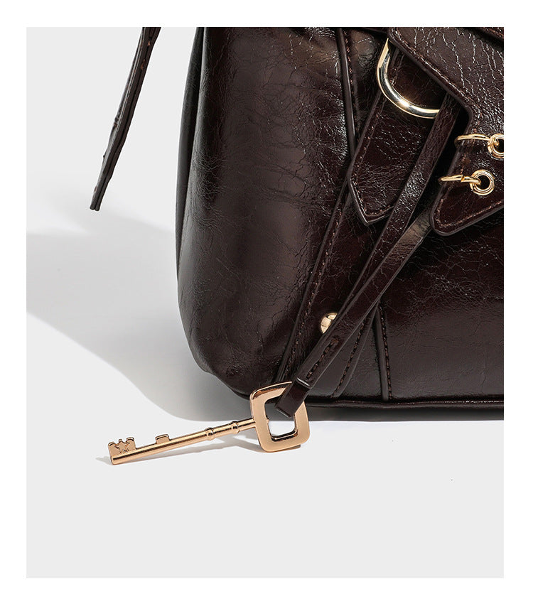 Dark brown glossy crinkled leather-look barrel bag with gold heart lock, dome studs, star charm, dual top handles and, detail