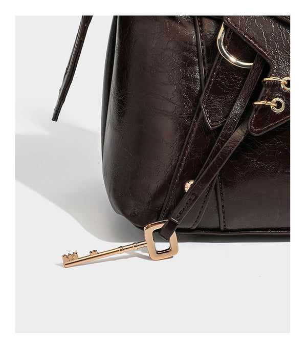 Dark brown glossy crinkled leather-look barrel bag with gold heart lock, dome studs, star charm, dual top handles and, detail