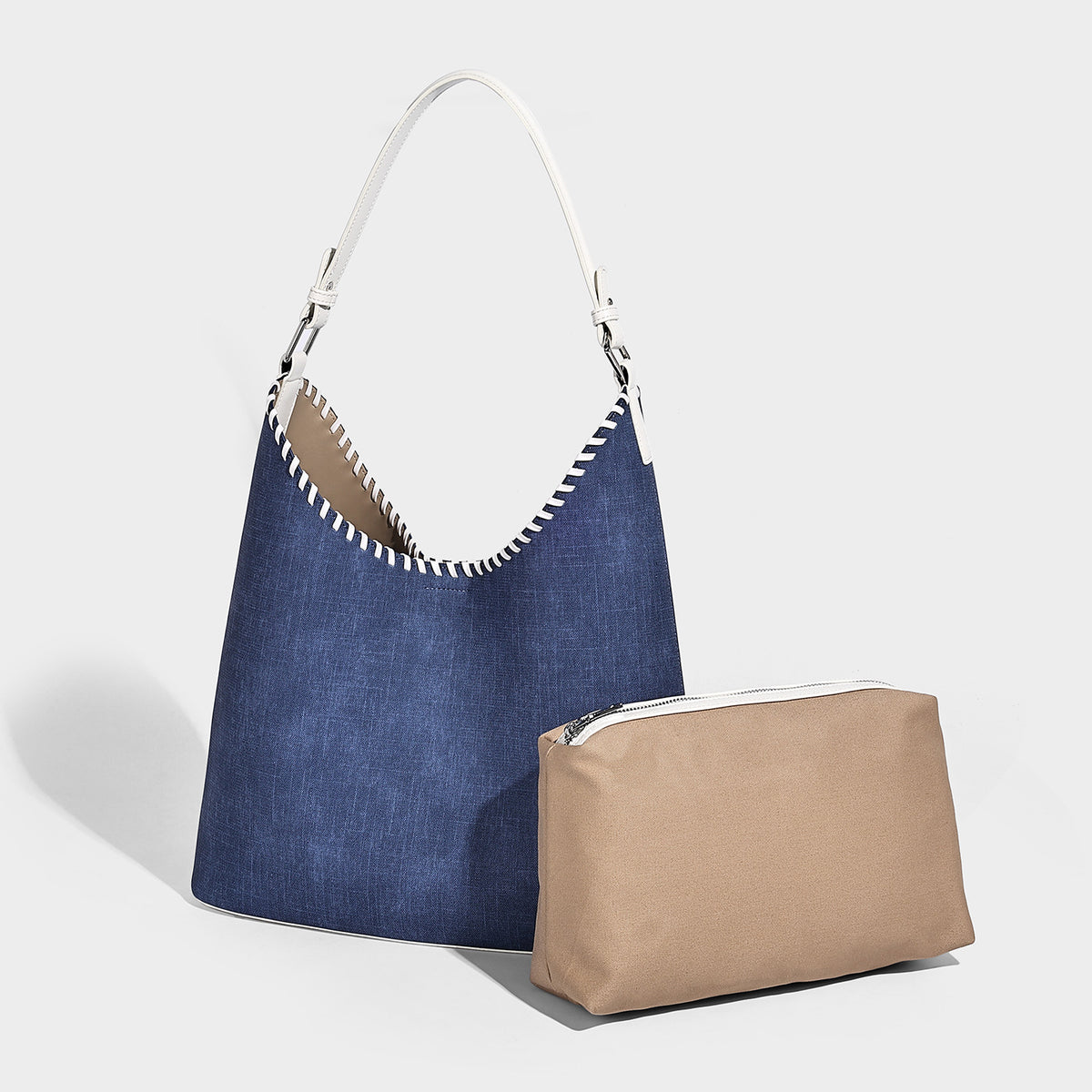 Denim-blue hobo tote with white leather-look shoulder strap, contrast whipstitch trim along curved open top, and silver-tone
