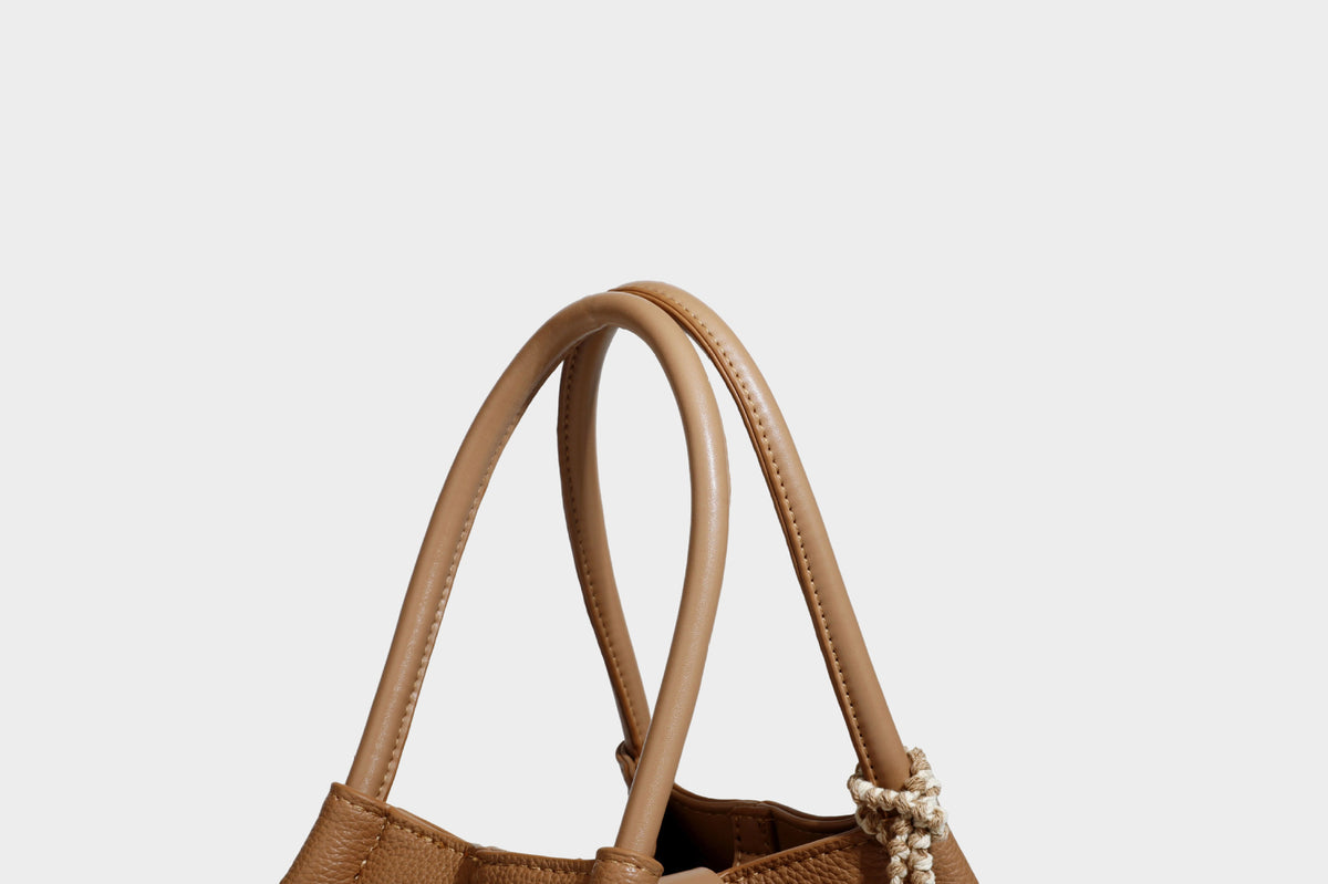 Pebbled leather-look bucket tote bag with rolled double handles, drawstring closure, braided cord charm, and detachable