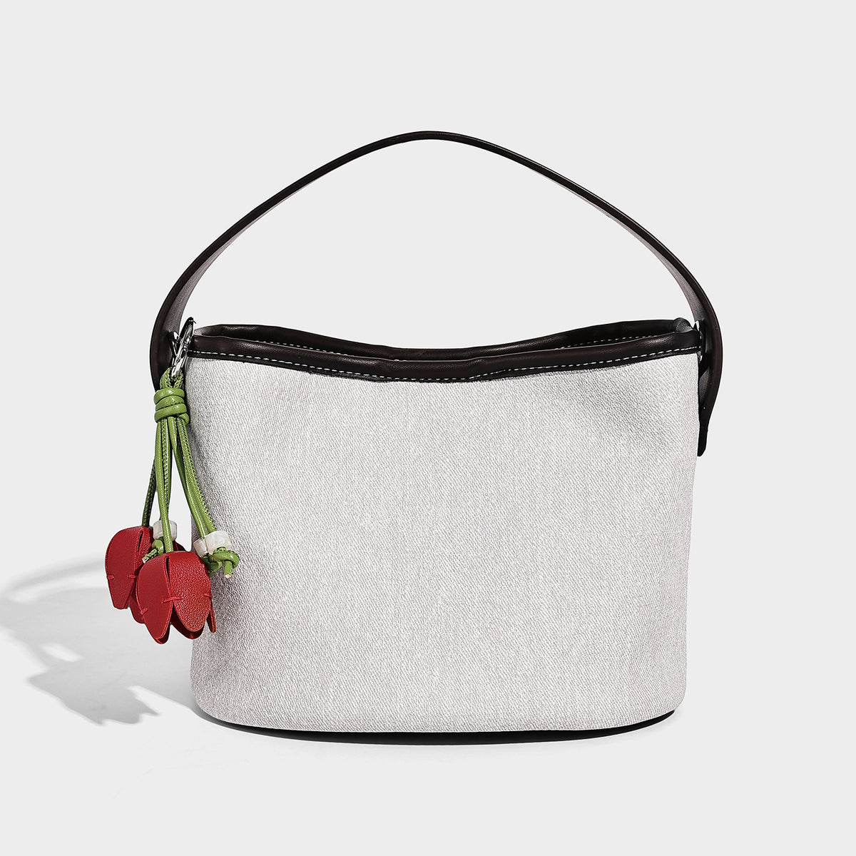 Small denim-look bucket bag with black leather-look trim, pink tulip flower charm, and adjustable crossbody strap, detail