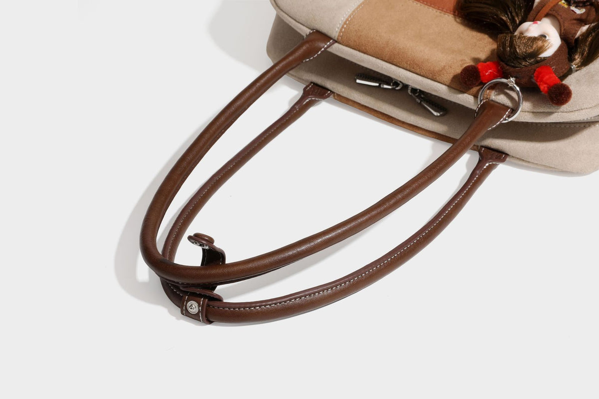 Boxy patchwork suede-look shoulder tote in tan, beige, rust, and brown panels with double brown straps and hanging doll