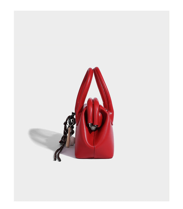 Small structured shell top-handle bag in red with heart charm and braided cord detail, smooth leather-look finish, detail