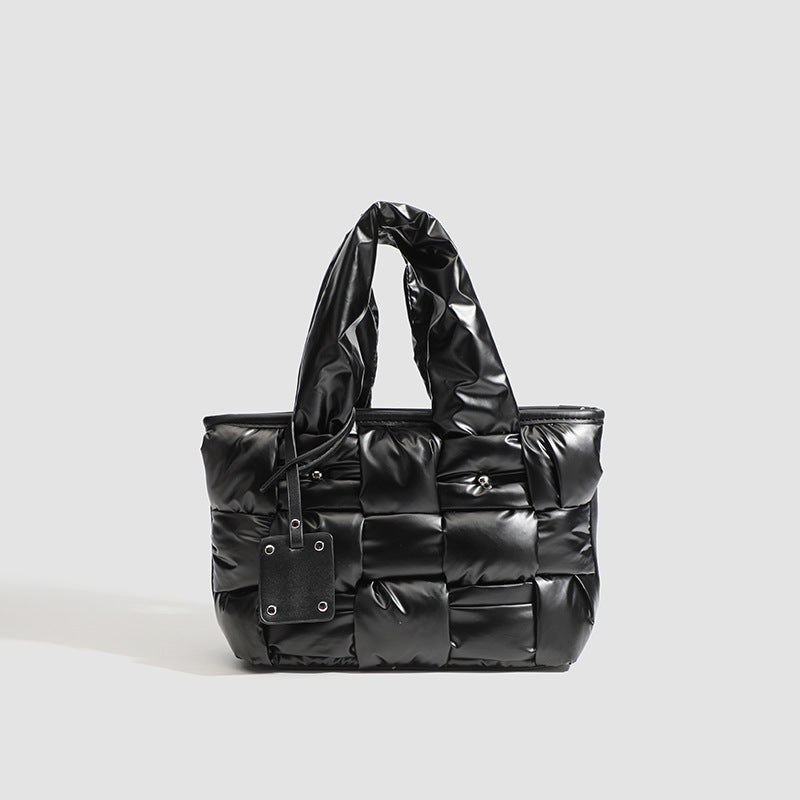 Black glossy woven puffer tote bag with padded top handles and detachable shoulder strap, front view