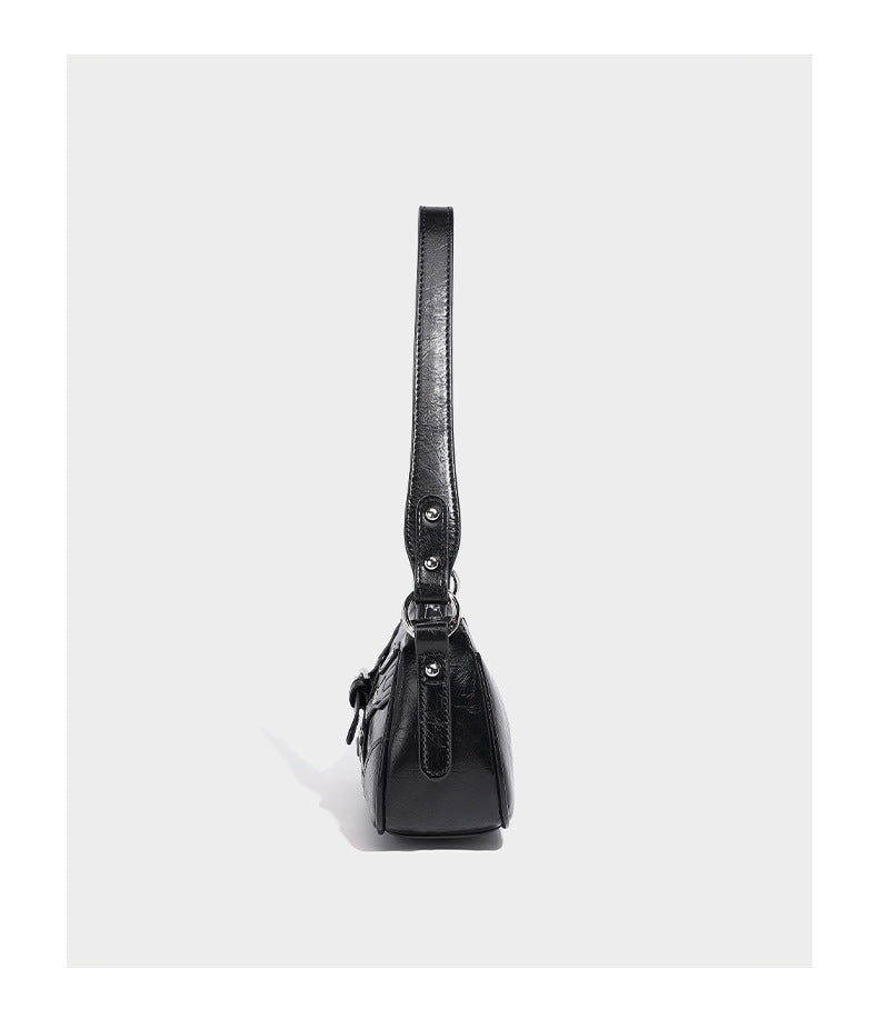 Compact moto-inspired shoulder bag with crisscross grommet strap detail, glossy textured finish, and adjustable crossbody