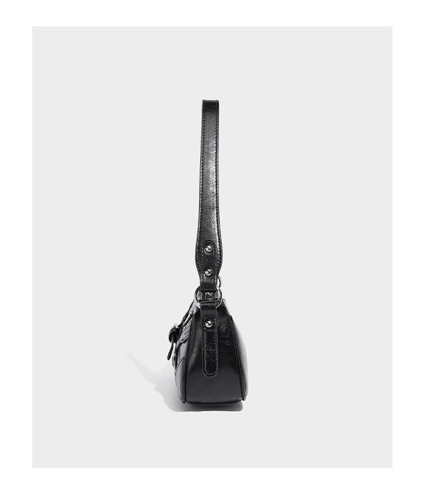 Compact moto-inspired shoulder bag with crisscross grommet strap detail, glossy textured finish, and adjustable crossbody
