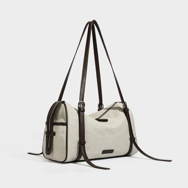 Beige canvas barrel bag with dark brown leather-look trim, silver-tone hardware, top zip closure, and adjustable shoulder