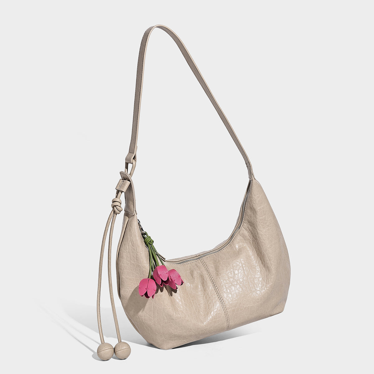 Slouchy crescent half-moon shoulder bag in pink pebbled textured finish with floral charm and knotted side detail, detail