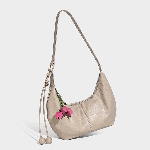 Slouchy crescent half-moon shoulder bag in pink pebbled textured finish with floral charm and knotted side detail, detail