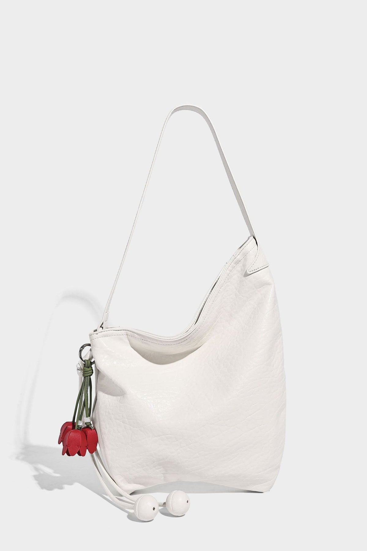 Slouchy hobo shoulder bag in pale yellow with slim strap, drawstring bead closure, and pink tulip floral charm, detail view
