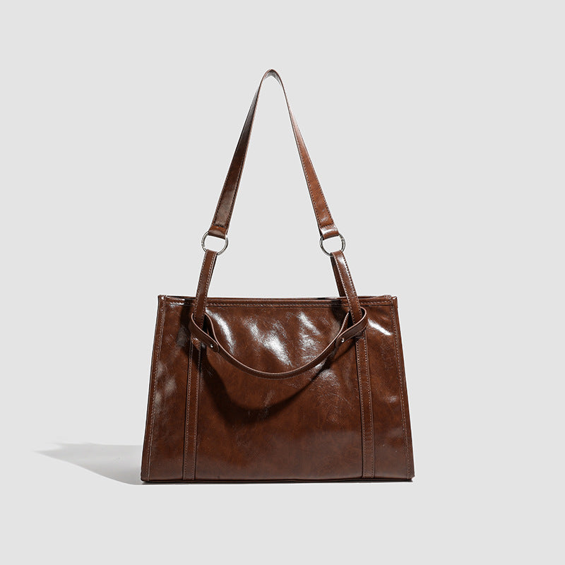 Large structured glossy leather-look tote bag with dual top handles and long shoulder strap in burnished brown, detail view 6