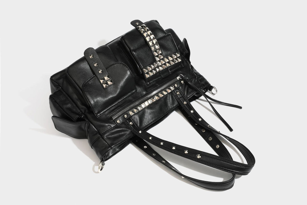 Black leather-look tote bag with silver pyramid studs on handles and front panel, multiple flap and zip exterior pockets