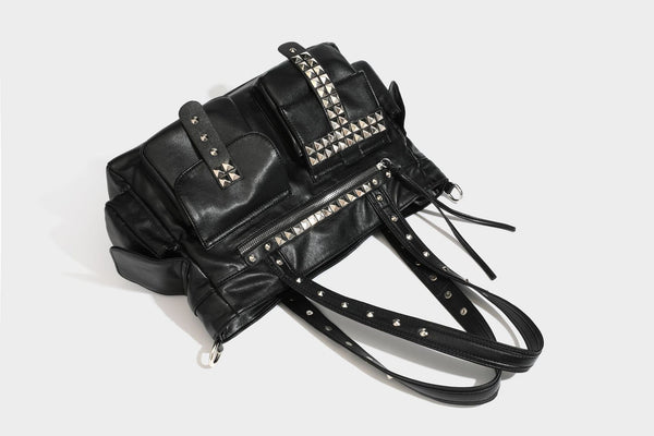 Black leather-look tote bag with silver pyramid studs on handles and front panel, multiple flap and zip exterior pockets
