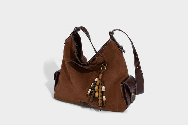 Lässig fallende Hobo-Schultertasche in Khaki aus mattem Material in Wildlederoptik mit dunkelbraunem Besatz in Lederoptik, Quastenanhänger mit Perlen und seitlicher Klappe, Detailansicht