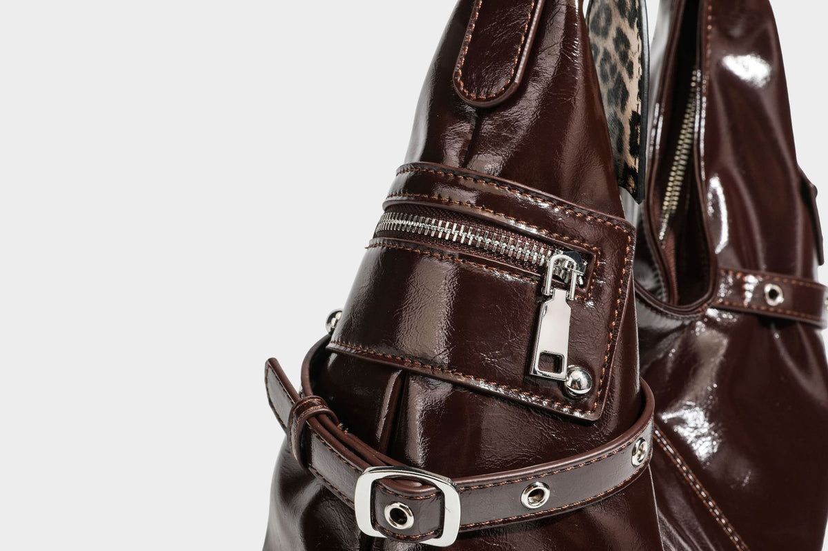 Glänzende dunkelbraune, lässig geschnittene Hobo-Schultertasche mit Riemendetail mit silberfarbenen Ösen, Reißverschlussfach auf der Vorderseite und Herz mit Leopardenmuster