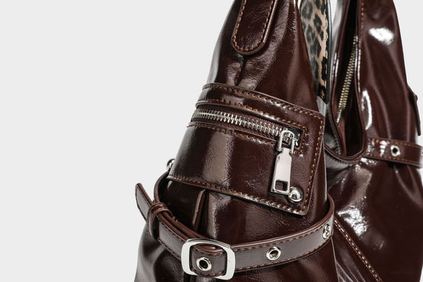 Glänzende dunkelbraune, lässig geschnittene Hobo-Schultertasche mit Riemendetail mit silberfarbenen Ösen, Reißverschlussfach auf der Vorderseite und Herz mit Leopardenmuster