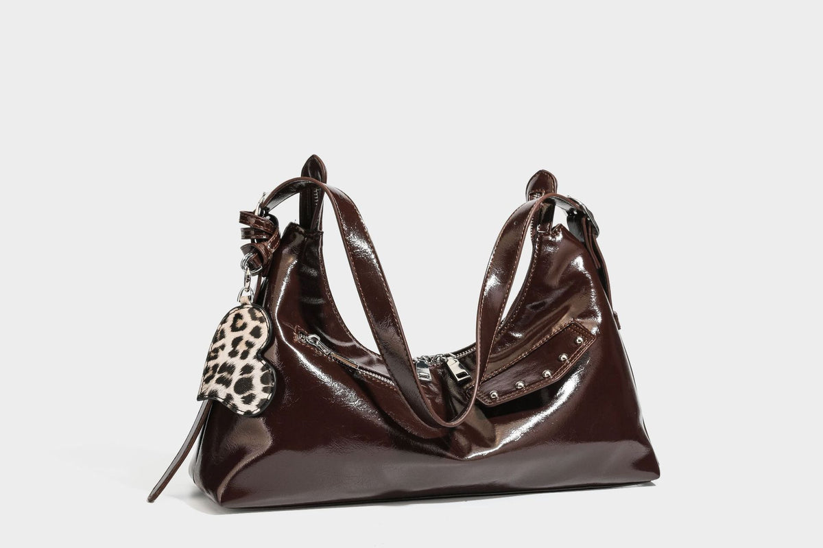 Glossy dark brown hobo shoulder bag with slim strap, front zip pocket, stud detail, and detachable leopard-print heart charm