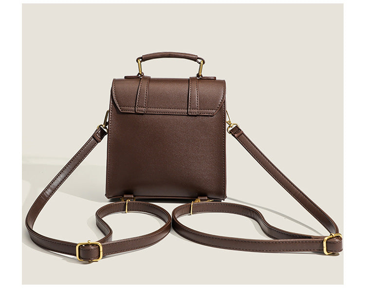 Structured mini satchel backpack with smooth leather-look finish, front flap pocket, gold-tone stud closures, and top handle