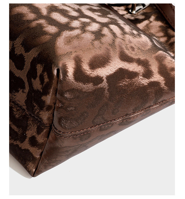 Glossy leopard-print tote bag with leather-look dark trim, dual top handles, detachable shoulder strap, and attached front