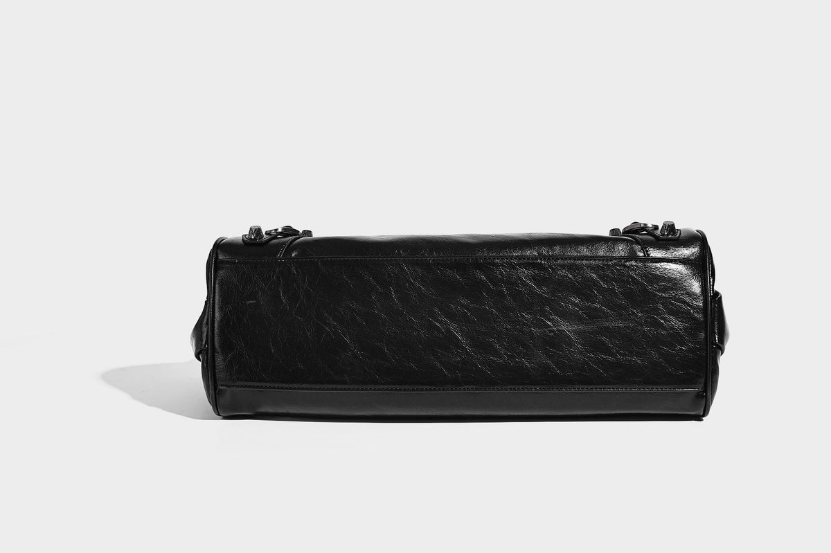 Längliche Schultertasche in Zylinderform mit glänzender Lederoptik, silberfarbenen Nietenbeschlägen, seitlichen Quasten und mehreren außenliegenden Reißverschlüssen