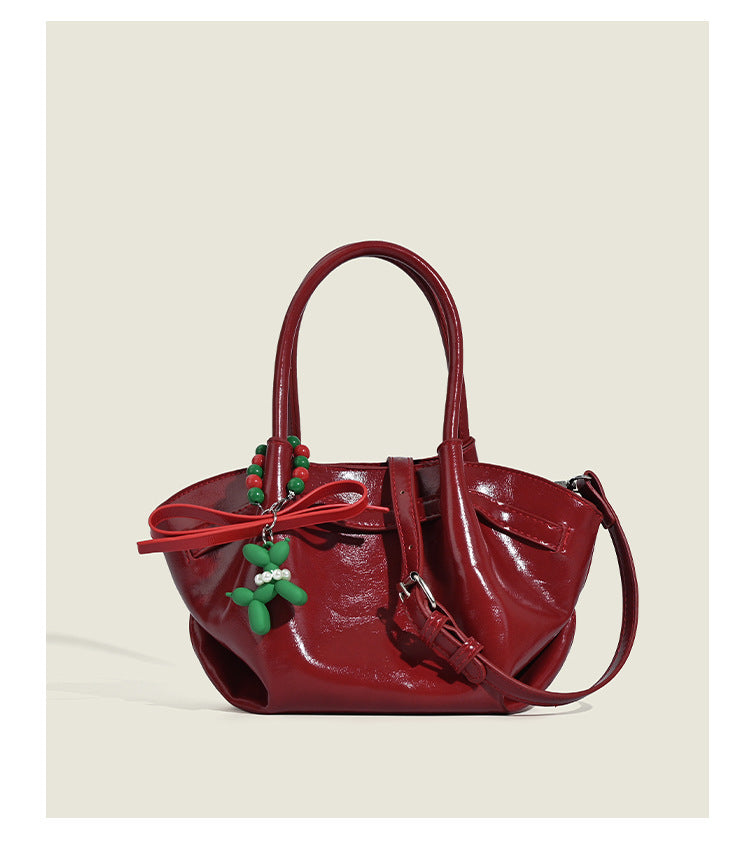 Small structured red glossy PU handbag with bow-and-bead charm, dual top handles, and detachable crossbody strap, detail view