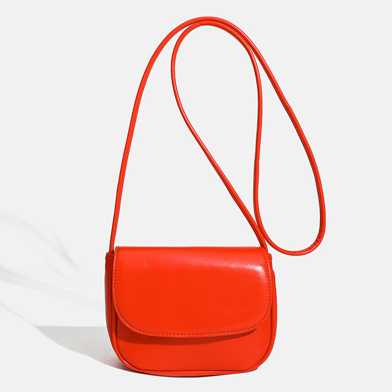 Compact rounded rectangular flap crossbody bag with glossy leather-look finish and long shoulder strap, front view