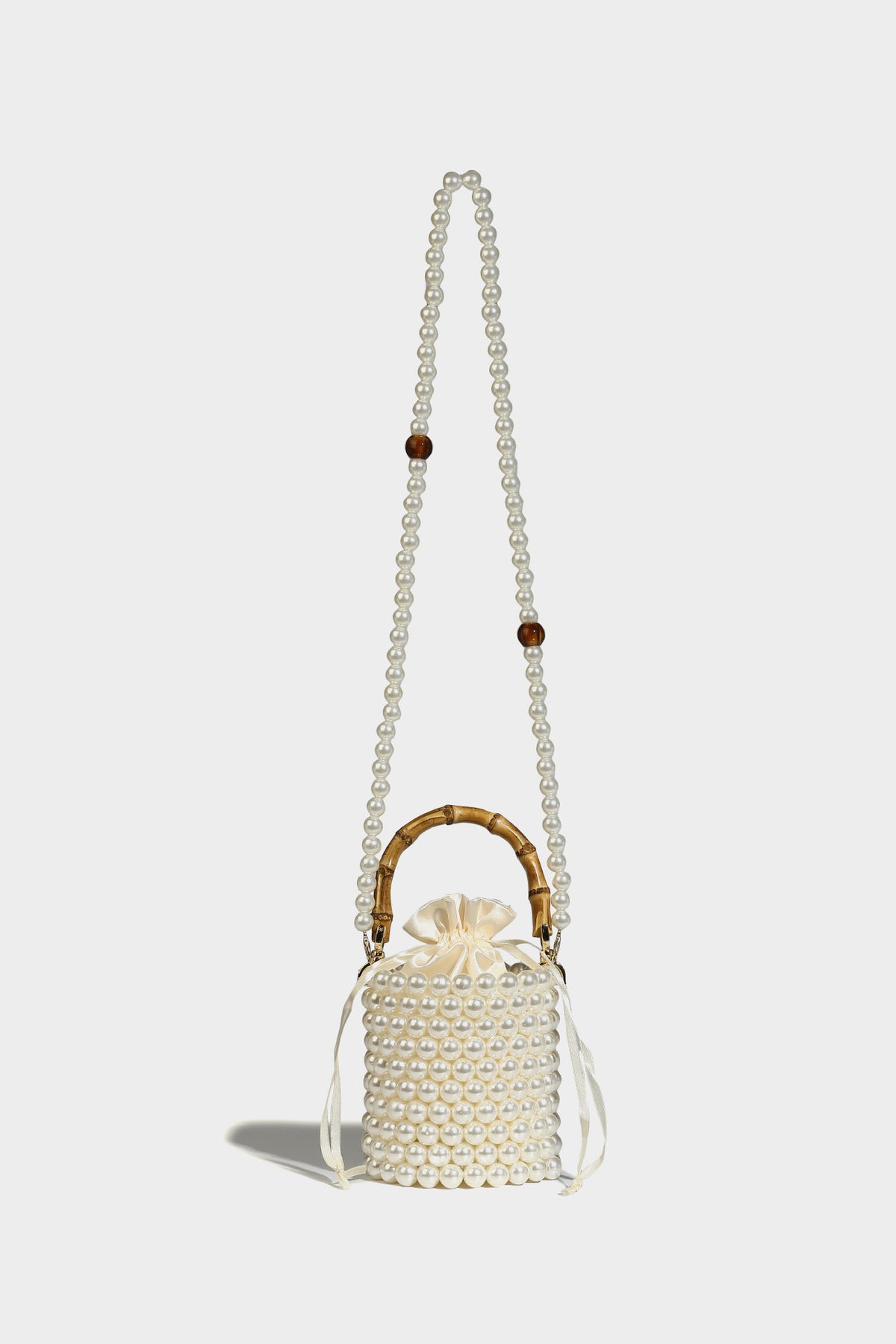 Small cylindrical bucket bag with glossy faux-pearl bead exterior, bamboo arched top handle, satin drawstring closure, and
