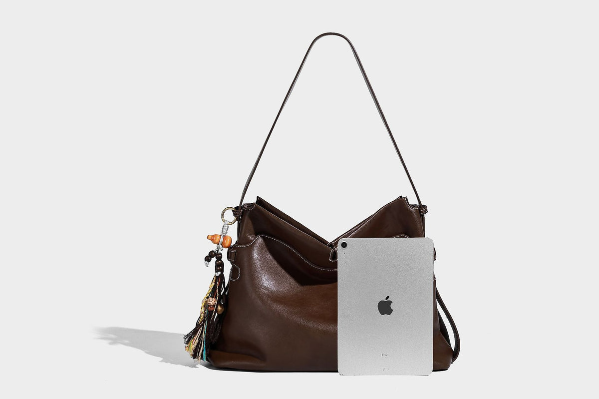 Large slouchy leather-look hobo tote bag with open top, adjustable shoulder strap, and colorful tassel bead charm, detail