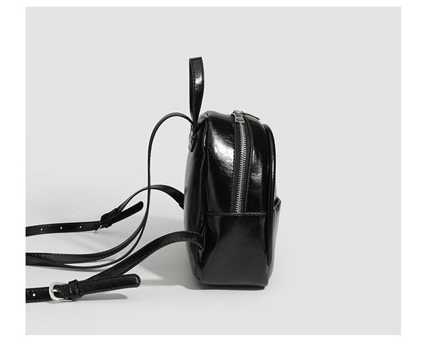 Kompakte, abgerundete Mini-Rucksackhandtasche mit glänzender Lederoptik, Reißverschluss oben, Fronttasche, Tragegriff oben und Detailansicht