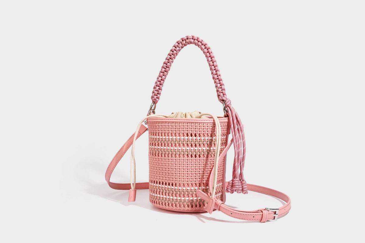 Detailansicht einer zylindrischen, handgeflochtenen Beuteltasche mit geflochtenem Henkel, Kordelzugverschluss, Kordelquasten und Metallringbeschlägen