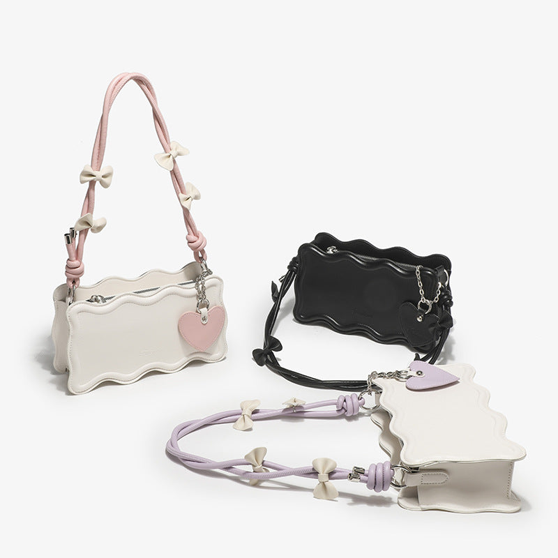 Small structured scalloped-edge shoulder bag with bow-tied pink cord strap and silver heart charm pendant, detail view 2
