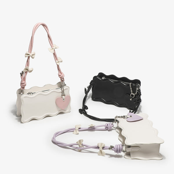 Small structured scalloped-edge shoulder bag with bow-tied pink cord strap and silver heart charm pendant, detail view 2