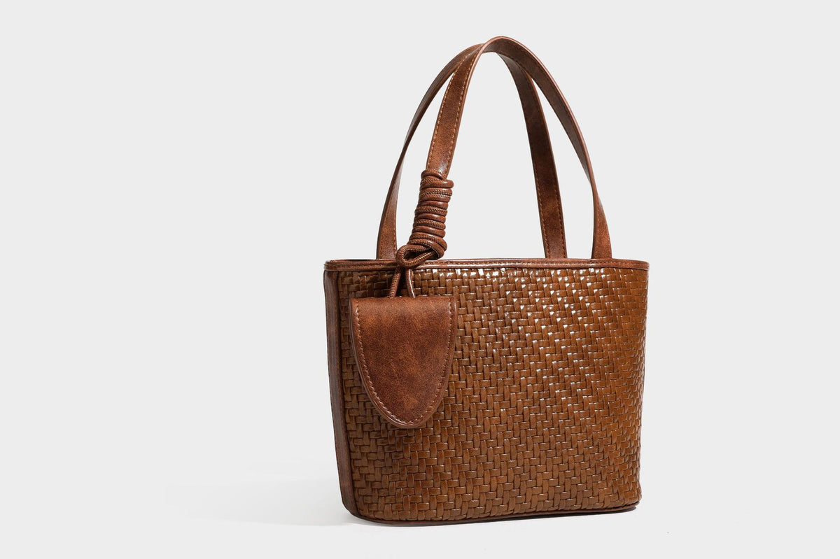 Strukturierte Tote Bag mit gewebter Oberfläche in Braun, goldfarbenen Metalldetails, seilumwickelten Tragegriffen, einer kleinen Fronttasche und weiteren Details