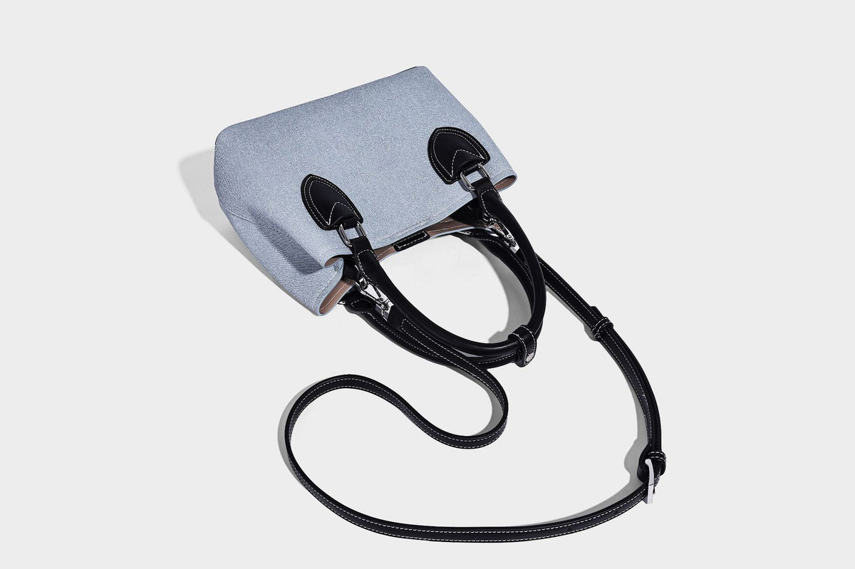 Structured light-blue denim-look tote bag with black leather-look handles, white contrast stitching, silver-tone hardware