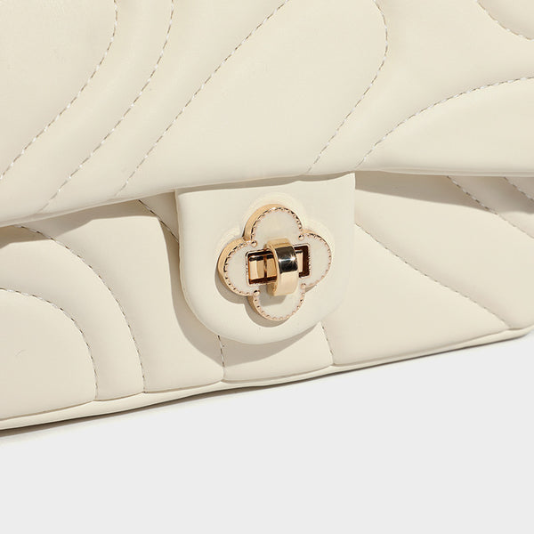 Compact cream quilted flap crossbody bag with wave stitching, gold-tone chain strap, and four-petal turn-lock clasp, detail