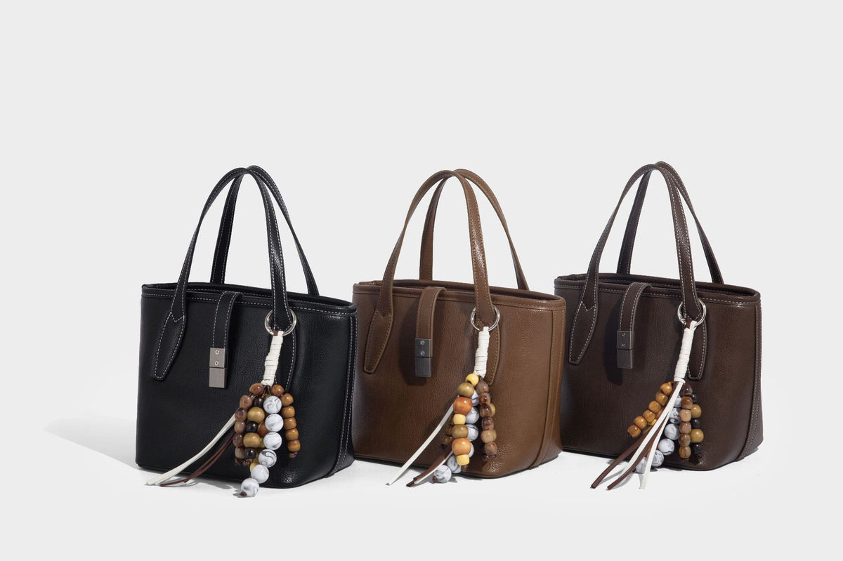 Compact structured bucket tote bag with pebbled textured finish, dual top handles, silver-tone lock hardware, and detachable