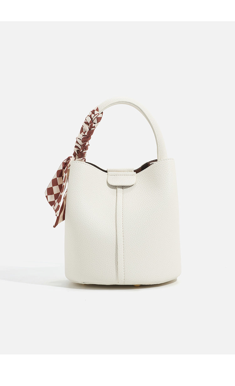 Pebbled leather-look bucket bag with checkered scarf-wrapped top handle, flap tab closure, gold-tone hardware, and matching